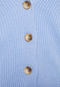 Light blue knitted cardigan featuring vertical ribbing and three round, brown buttons along the front. Soft texture and classic design.