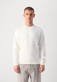Light beige crewneck sweatshirt made of soft fabric, featuring a subtle logo on the chest, ribbed cuffs, and a relaxed fit.