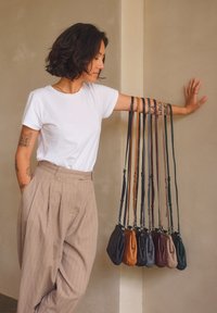 Borse a tracolla in pelle di diversi colori (nero, marrone, verde, arancione) con cinghie regolabili appese a un braccio, che mostrano il loro design e le texture.