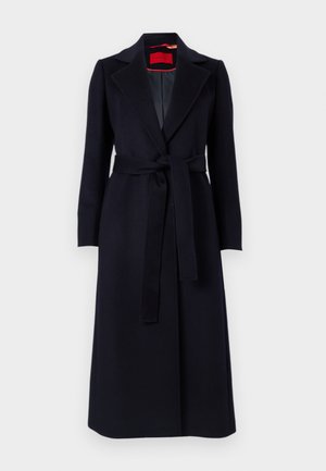 Μακρύ μαύρο παλτό από μάλλινο ύφασμα με ζώνη, γιακά με εγκοπές και κόκκινη εσωτερική επένδυση που φαίνεται στον γιακά, απεικονίζεται σε λευκό φόντο.