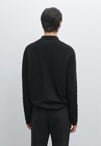 Schwarzer gestrickter Pullover mit langen Ärmeln und rundem Halsausschnitt, der eine weiche Textur und eine lockere Passform aufweist, von hinten betrachtet.