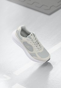 Chaussure de sport gris clair avec des panneaux en maille, un col rembourré et une semelle blanche texturée avec un accent noir sur le bout.