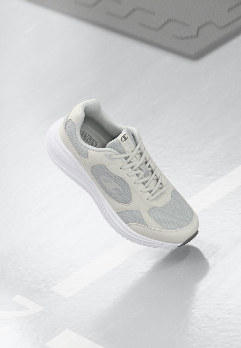 Chaussure de sport gris clair avec des panneaux en maille, un col rembourré et une semelle blanche texturée avec un accent noir sur le bout.