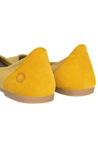 Žluté semišové boty s špičatou špičkou a minimalistickým designem. Mají hnědou gumovou podrážku a decentní logo na straně.