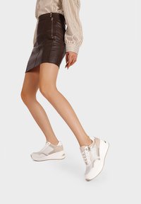 Zapatillas para mujer en una combinación de color beige claro y blanco, que combinan materiales de cuero y malla, con una suela de cuña y detalles de cremallera.