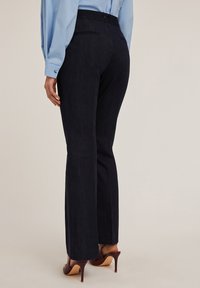 Donker denim flarebroeken met een hoge taille en twee achterzakken, gecombineerd met een lichtblauwe blouse met lange mouwen en bruine hoge hakken.