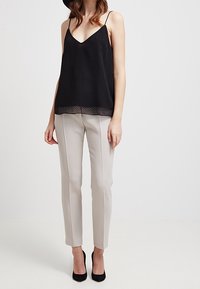 Zwarte spaghettibandjes camisole met stippenpatroon, gelaagde onderzoom, gecombineerd met lichtgrijze op maat gemaakte broeken en zwarte hoge hakken.