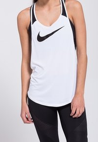 Débardeur Nike blanc avec accents noirs et logo bien visible. Présente un col arrondi et un dos nageur. Associé à des leggings noirs.