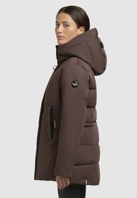 Brown puffer coat with a hood, featuring a zippered front, side pockets, and a logo accent on the sleeve. Smooth, padded texture.