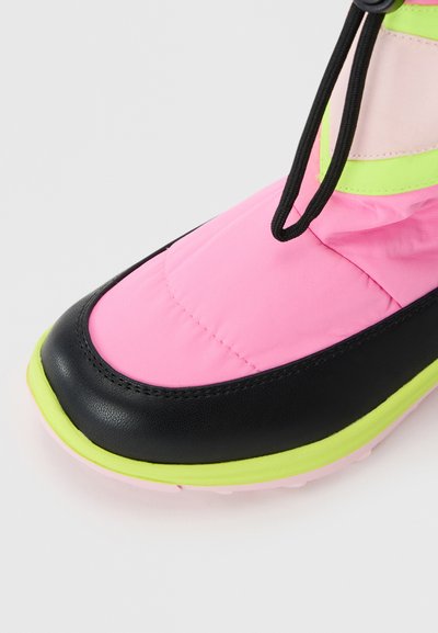 Sapatilha rosa e preta com detalhe de sola neon amarela e atacadores elásticos pretos, em close na zona do bico contra um fundo branco.