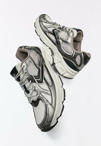 Paire de chaussures de course grises et noires avec semelles blanches, panneaux en mesh et lacets sur fond blanc.