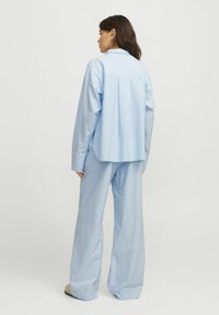 Gaiši zils, garām piedurknēm krekls ar aizmugures plisējumam, apvienots ar brīviem, atbilstošiem svītrainajiem biksēm. Gluda tekstūra, ikdienas piegriezums.