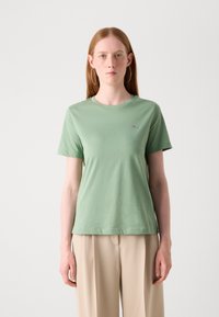 T-shirt in cotone verde menta con colletto rotondo, maniche corte e un piccolo logo sulla parte sinistra del petto. Texture liscia.