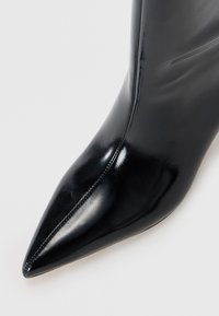 Stivaletto in pelle nera con punta affusolata, caratterizzato da una finitura lucida e un dettaglio nella cucitura laterale. Design elegante e raffinato.
