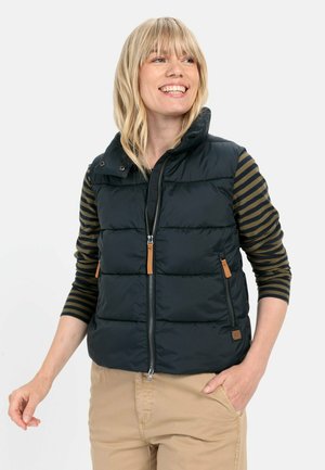 Black puffer vest with high collar, front zipper, and two zippered pockets. Accents include tan leather patches and decorative stitching.