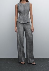 Szara lniana bluzka bez rękawów o subtelnej teksturze, zestawiona z luźnymi spodniami w tym samym kolorze. Noszona z prostymi czarnymi sandałami.