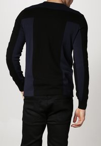 Pull en tricot avec panneaux noirs et bleu marine, encolure ronde, poignets et ourlet côtelés. Texture lisse, silhouette ajustée et couleur unie.