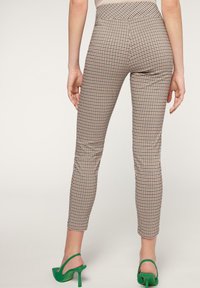 Bruna och beige rutiga leggings med hög midja, med en elegant design, som matchas med gröna högklackade sandaler.