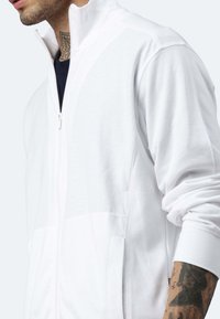 Weiße zip-up Jacke mit hohem Kragen und weichem, strukturiertem Stoff. Verfügt über Seitentaschen und sichtbare Nähdetails.