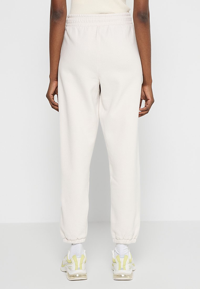 Jasno beżowe dresy z elastycznym pasem i ściągaczami na nogawkach. Wykonane z miękkiego materiału, charakteryzujące się luźnym krojem i minimalistycznym wzornictwem.