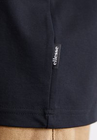 Marineblå bomull T-skjorte med teksturfinish, med en liten svart etikett med "ellesse" trykt i hvitt på sidesømmen.