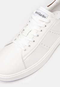 Weiße Leder-Sneaker mit Schnürdesign, durchbrochenen Akzenten an der Seite und einer weißen Gummisohle. Verfügt über ein Logo auf der Zunge.