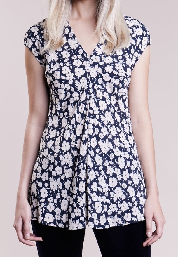 Blommig blus med marin bakgrund, korta ärmar, V-hals och rynkor i mitten. Har vita blommor över hela tyget.