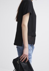 Svart kortärmad topp med lagerdesign, kombinerad med ljusblå denim och en svart clutch-väska med fransdetaljer.