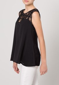 Schwarzes ärmelloses Oberteil mit Spitzenbesatz am Ausschnitt, das eine lockere Passform, glattes Material und einen abgerundeten Saum aufweist.