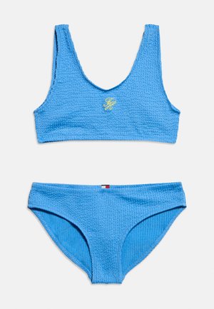 Set de bikini albastru texturat cu sutien sport cu inițiale brodate galbene și slipuri asortate cu croială înaltă și detaliu mic de steag.