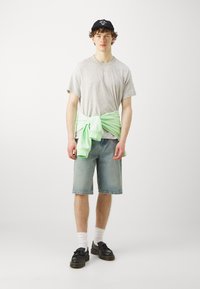 Gray t-shirt, light green sweatshirt tied at the waist, blue denim shorts, black shoes, and white socks on a plain background.