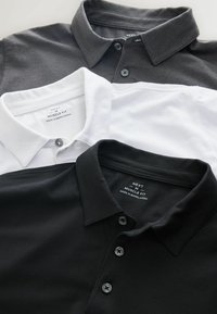 Drei Poloshirts in Schwarz, Weiß und Grau, aus weichem Baumwollstoff, mit Kragen und Knopfverschluss, übereinander gestapelt.