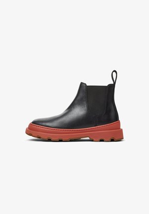 Botte cheville en cuir noir avec des panneaux latéraux élastiques, semelle en caoutchouc rouge et tirant ; design épuré avec un bout arrondi et des accents texturés.