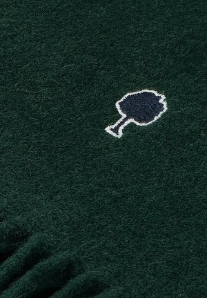 Groene wollen stof met een zachte textuur, voorzien van een geborduurd boompictogram in wit en marineblauw. Gerimpelde randen aan de onderkant.