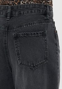 Black denim jeans featuring a single back pocket with a square shape, sturdy stitching, and a slight washed texture.