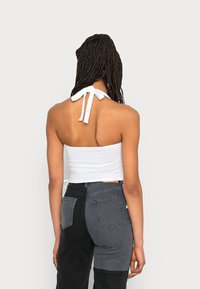 Top halter branco com as costas abertas, preso com uma fita. Usado com jeans em bloco de cores preto e cinza, apresentando bolso distinto.