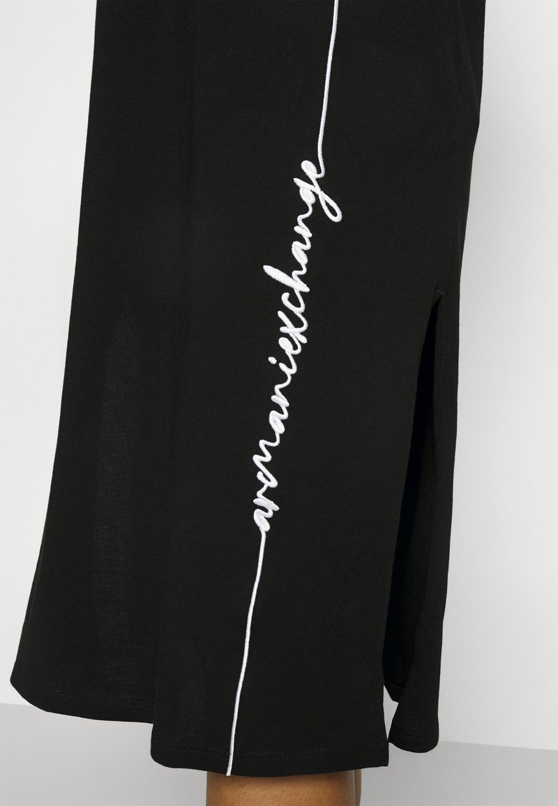 Falda negra hecha de tela suave con una abertura lateral. Presenta texto bordado en blanco a lo largo de la costura izquierda. Diseño simple y de corte recto.