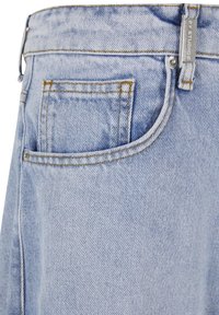 Világoskék farmer zseb narancssárga varrással és ezüst szegeccsel, melyen egy fém címke olvasható: "A.P.C. STUDIOS."