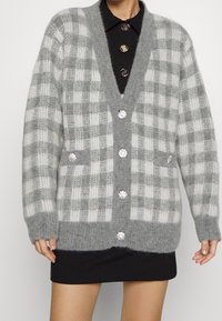 Grå och vit rutmönstrad cardigan med djup V-ringning, stora knappar, två framfickor och en mjuk, fluffig textur.