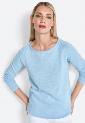 Top azzurro chiaro a maniche lunghe con colletto rotondo, tessuto morbido e testurizzato, e maniche raglan, con un sottile orlo sfilacciato.