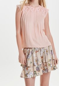 Blusa de melocotón con detalles de encaje en el hombro, combinada con una falda rizada floral beis que presenta patrones florales multicolores.