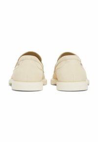 Par af beige slip-on sko med hvide såler vist fra bagsiden på en hvid baggrund.
