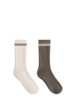 Une chaussette beige et une marron côtelée avec des points antidérapants sous la semelle, chacune avec deux bandes horizontales près du haut.