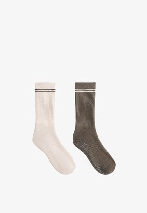 En beige og en brun ribstrikket sok med grebpunkter på sålen, hver med to horisontale striber nær toppen.
