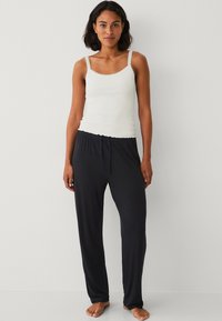 Witte tanktop met kantafwerking en zwarte drawstring broek, met een ontspannen pasvorm en een soepele textuur, geschikt voor loungewear of slaapkleding.
