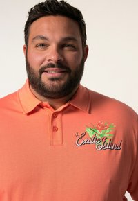 Korálová poloshrnutí s límečkem, zdobená tropickým vzorem rostlin a vyšitým nápisem "Exotic Island" v černé barvě. Hladká bavlněná textura.