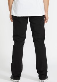 Jeans din denim negru cu croială dreaptă, având buzunare și cusături în contrast, asortați cu adidași Converse negri și albi.