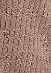 Gebreide stof in een zachte taupekleur met een verticale geribbelde structuur. Heeft gladde stiksels en een subtiele glans.