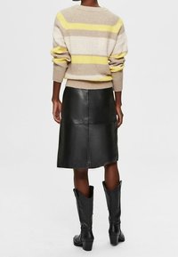 Beige gestrickter Pullover mit gelben und taupefarbenen Streifen, kombiniert mit einem schwarzen Lederrock. Schwarze Cowboy-Stiefel runden das Outfit ab.