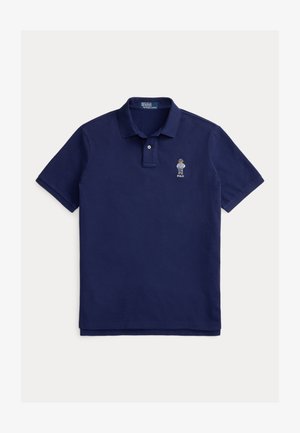 Μπλε σκούρο πόλο μπλουζάκι από βαμβάκι με κλείσιμο δύο κουμπιών. Διαθέτει κεντημένο έμβλημα στο αριστερό στήθος, κοντά μανίκια και ίσια γραμμή στο τελείωμα.